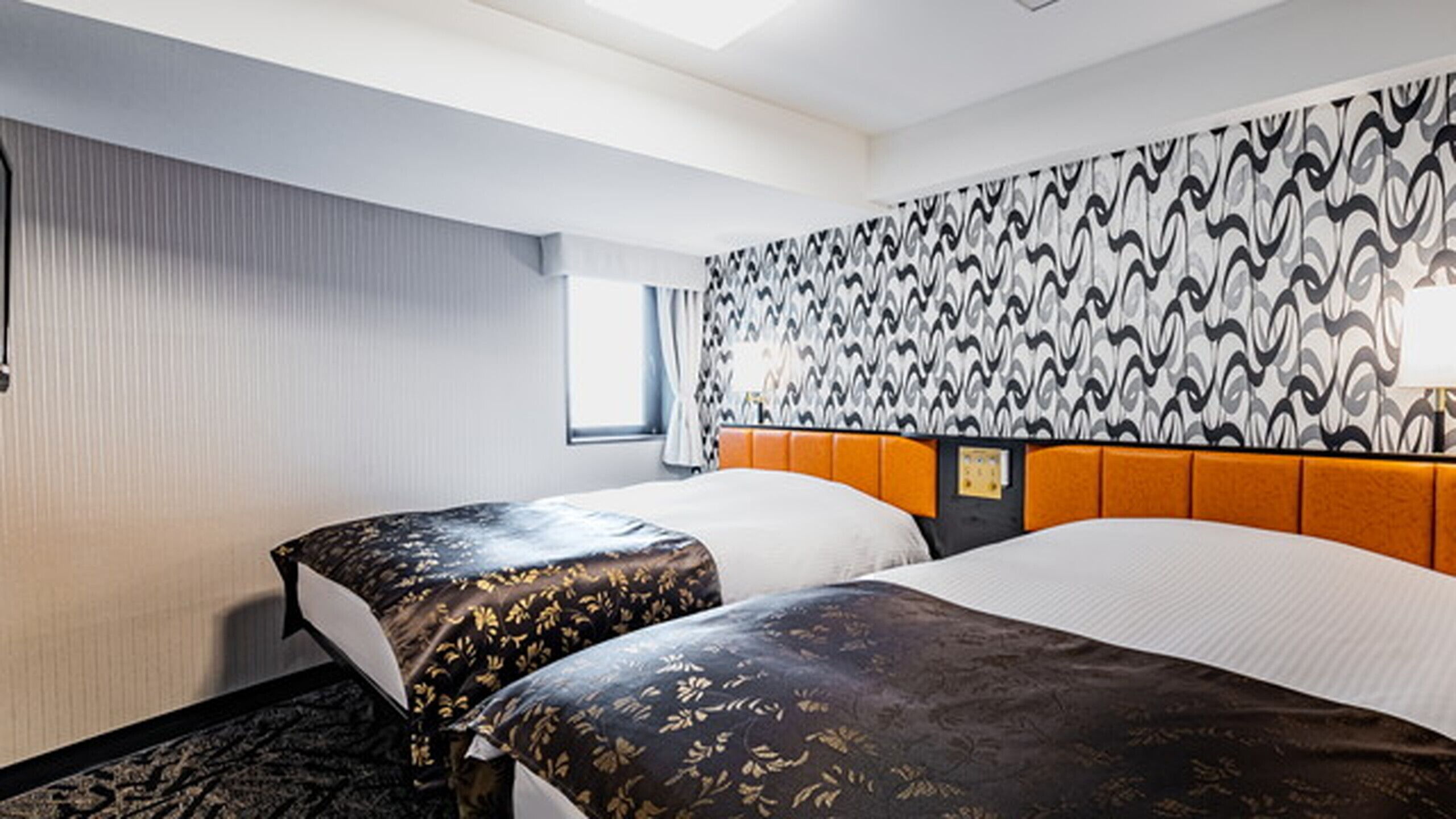 A hotel room with two beds, a patterned headboard, a window with curtains, and a wall with a wavy pattern.