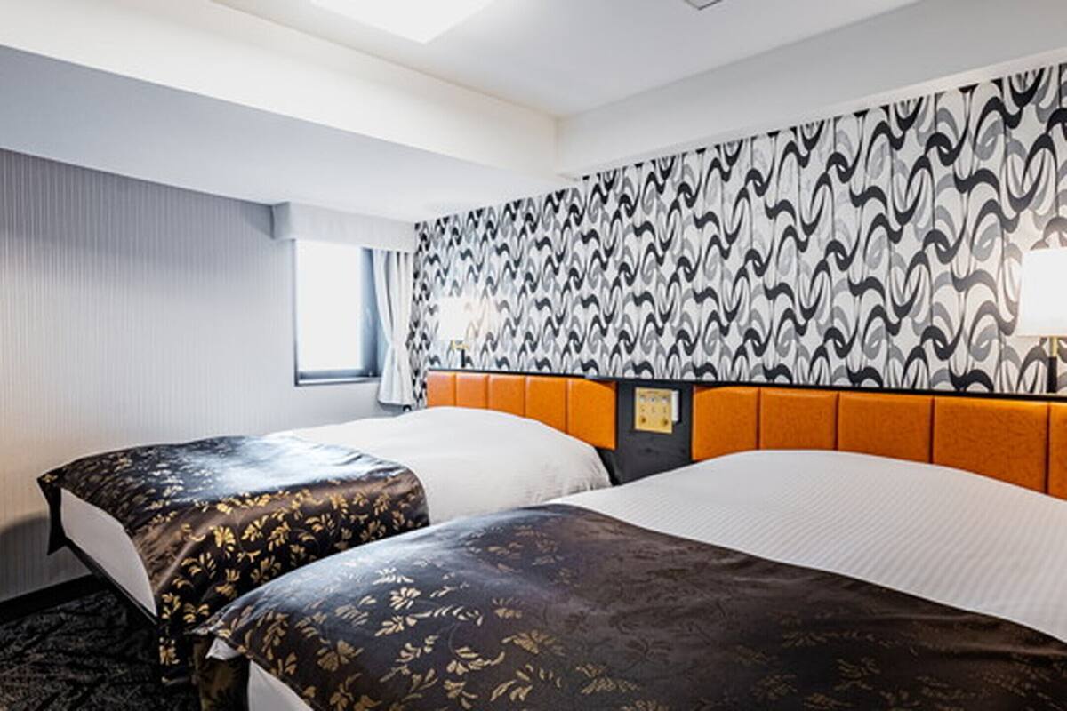 Ein Hotelzimmer mit zwei Betten, einem gemusterten Kopfteil, einem Fenster mit Vorhängen und einer Wand mit einem Wellenmuster.