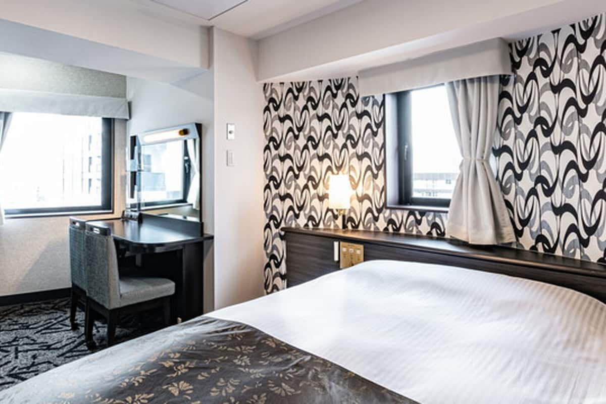 Ein Hotelzimmer mit Bett, Schreibtisch, Stuhl, Fenster und einer Wand mit Muster.