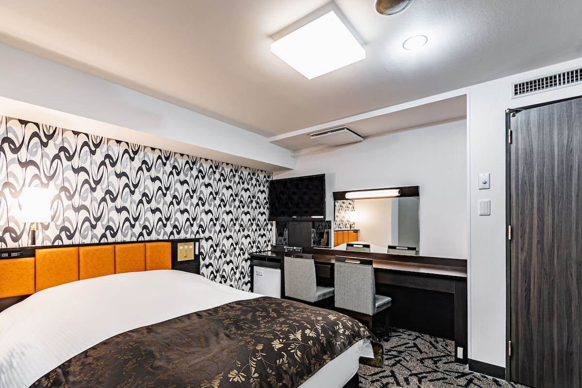 Ein Hotelzimmer mit einem großen Bett, einem Schreibtisch mit Stuhl, einem Fernseher und einem Kleiderschrank.