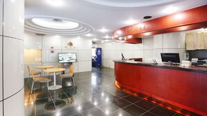 A hotel reception area with a red reception desk, a flat-screen TV, and a seating area with round tables and chairs. - APA Hotel Sapporo Hosui Susukino Ekimae (Sapporo)