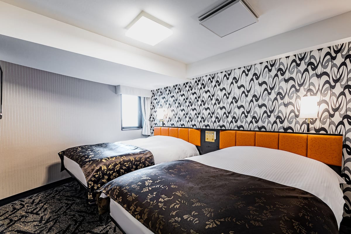 Ein Hotelzimmer mit zwei Betten, einer Wand mit Muster, einem Fenster mit Vorhängen und einer Deckenleuchte.