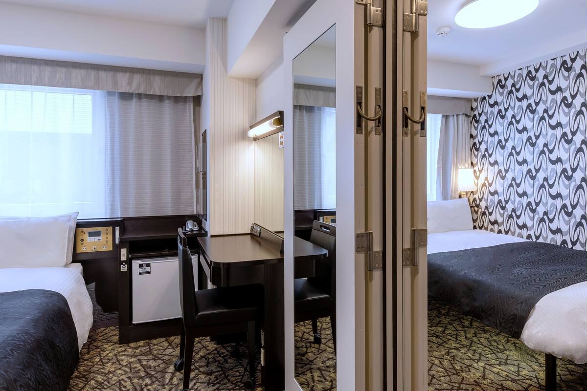 Ein Hotelzimmer mit zwei Betten, einem Schreibtisch, einem Stuhl, einer Schreibtischlampe, einem Telefon und einem Spiegel.