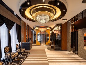 Een hotel lobby met een receptiebalie, zithoek en een weelderige kroonluchter.