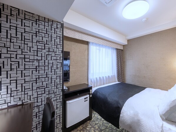Habitación de hotel con cama, escritorio, minibar, televisor y ventana con cortinas.