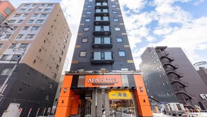 A tall hotel building with a modern design, featuring multiple balconies and a prominent orange and black facade. - APA Hotel Sapporo Odori Ekimae Nishi (Sapporo)
