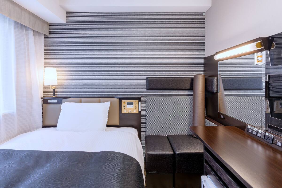Ein Hotelzimmer mit Bett, Nachttisch, Fernseher und Bedienfeld.