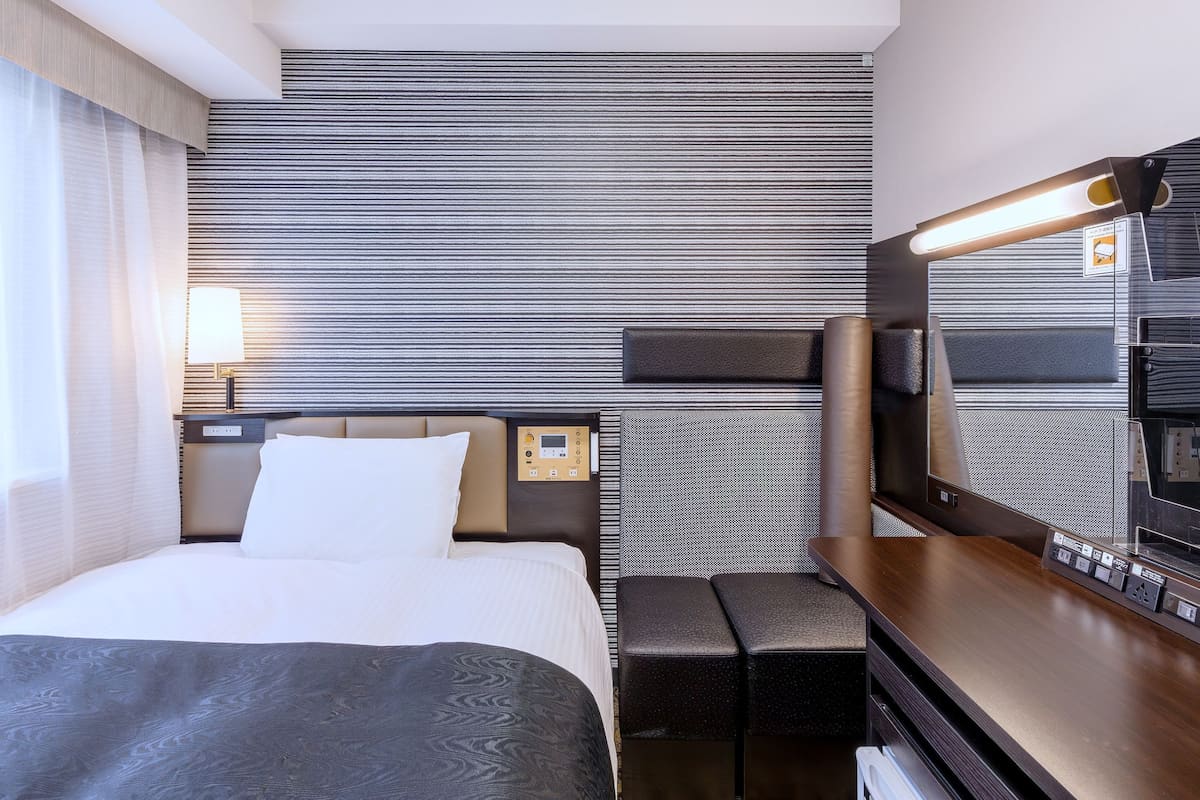 Une chambre d’hôtel avec un lit, une table de chevet, une lampe et un grand miroir.