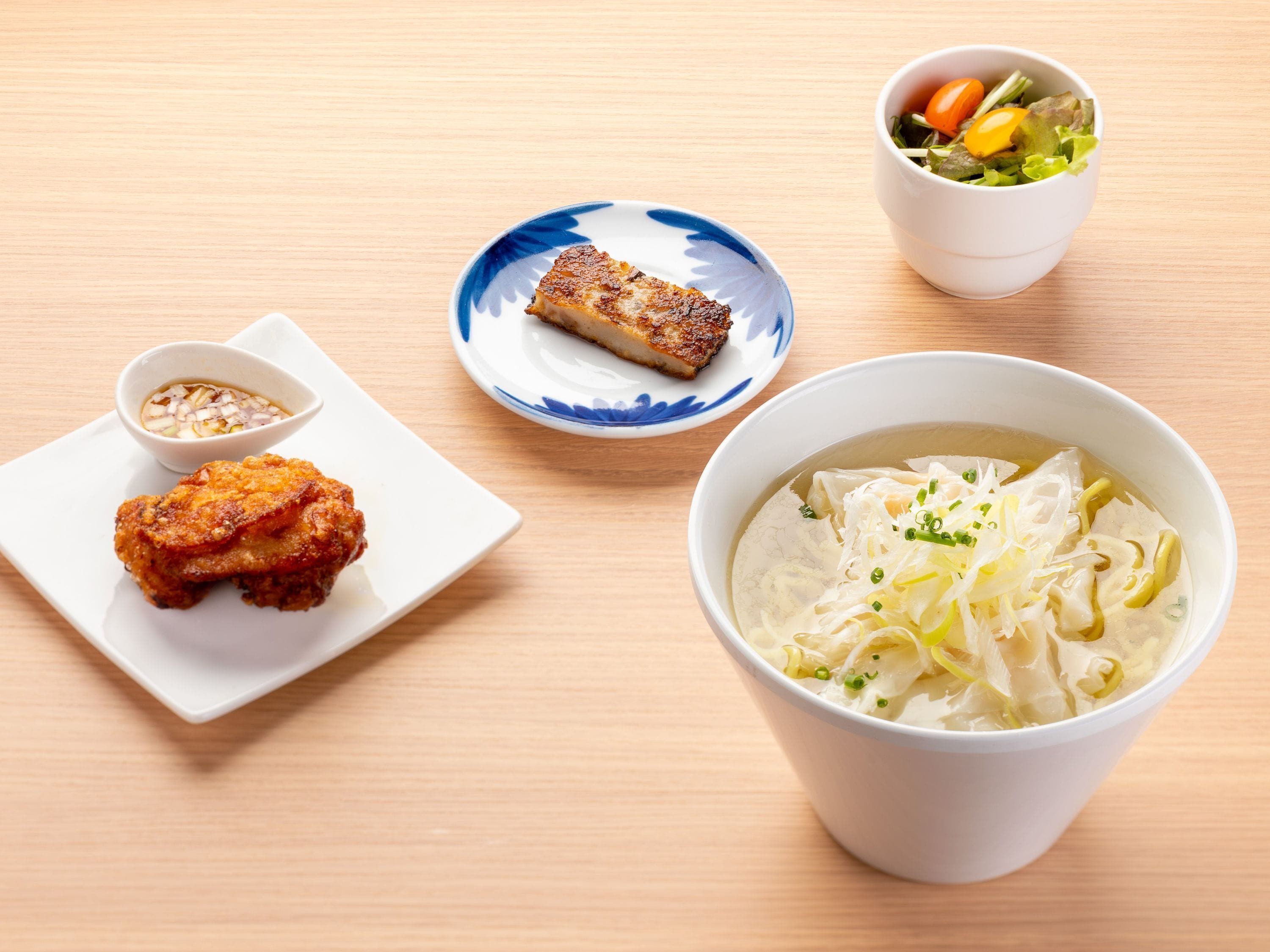 Une table avec un bol de soupe, une assiette contenant deux portions de nourriture frite, un petit bol de sauce pour tremper, et une assiette avec un morceau de viande grillée.
