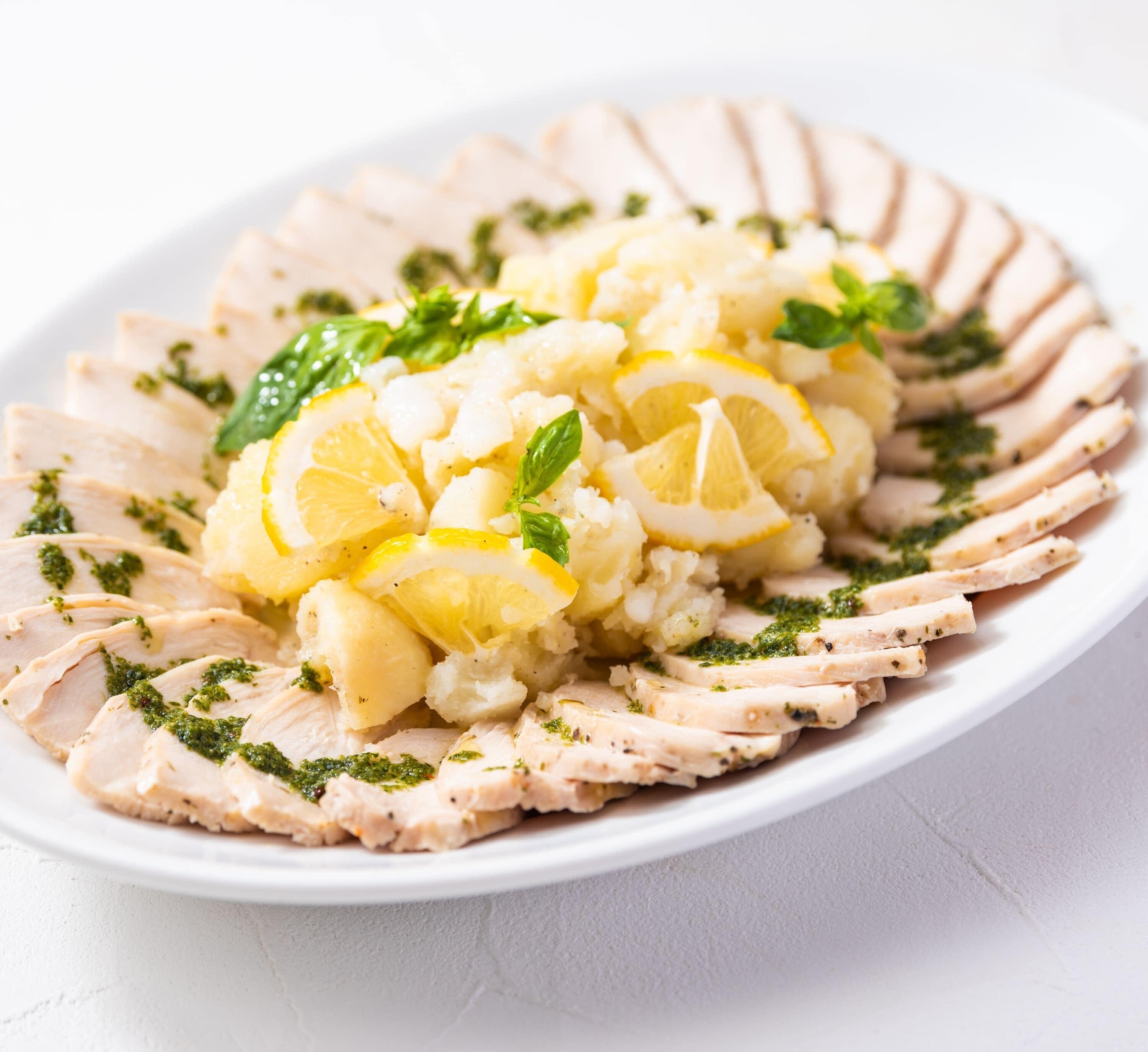 Une assiette de tranches de poulet, de rondelles de citron et de purée de pommes de terre, le tout garni d’herbes aromatiques.
