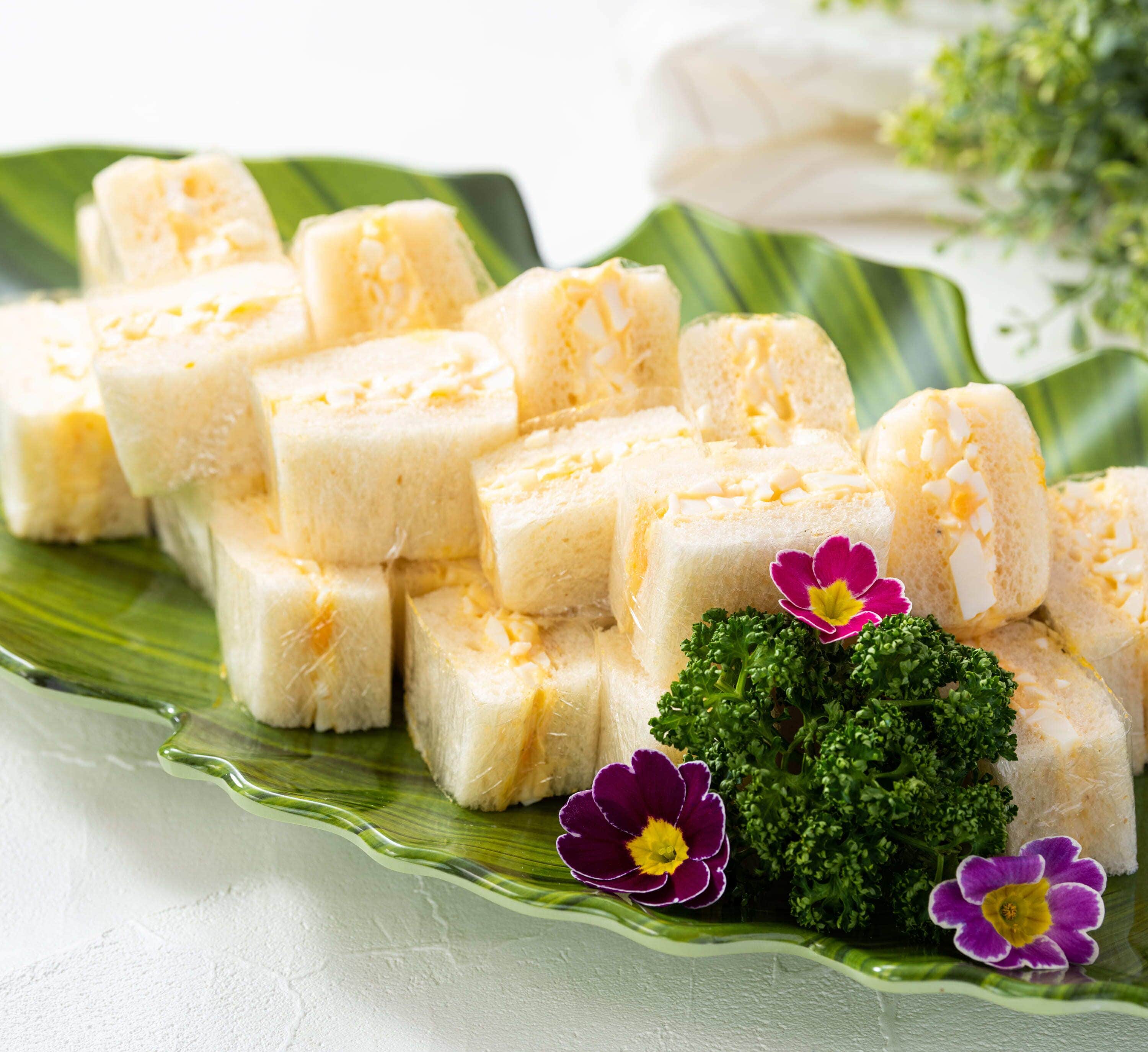 A plate of white, cubed food items with a green leaf and purple flowers.