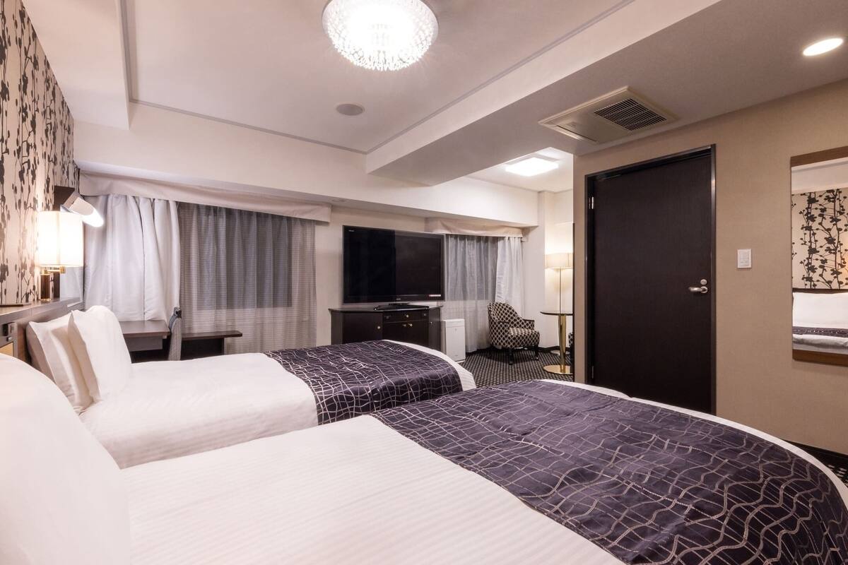 Ein Hotelzimmer mit zwei Betten, einem Schreibtisch, einem Fernseher und einer Tür.