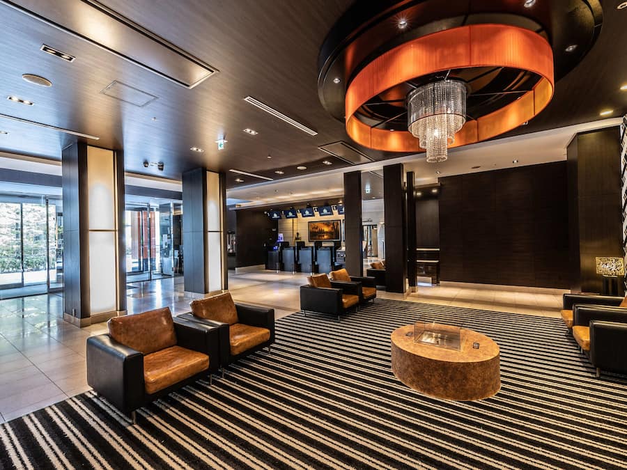 A modern lobby with a large chandelier, seating area, and a reception desk.