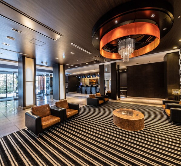 A modern lobby with a large chandelier, seating area, and a reception desk.