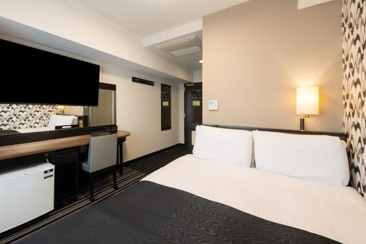 Une chambre d’hôtel équipée d’un lit, d’un bureau, d’une chaise, d’une télévision et d’une lampe fixée au mur.