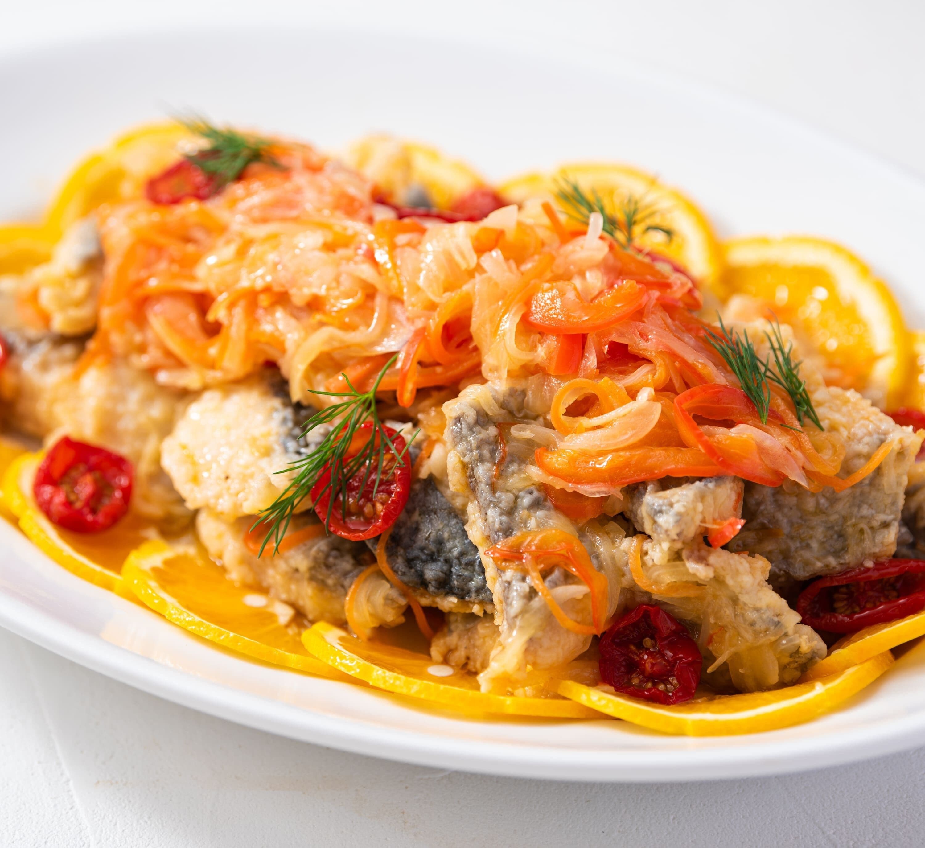 Ein Teller mit Fisch, Karotten und roten Paprika.