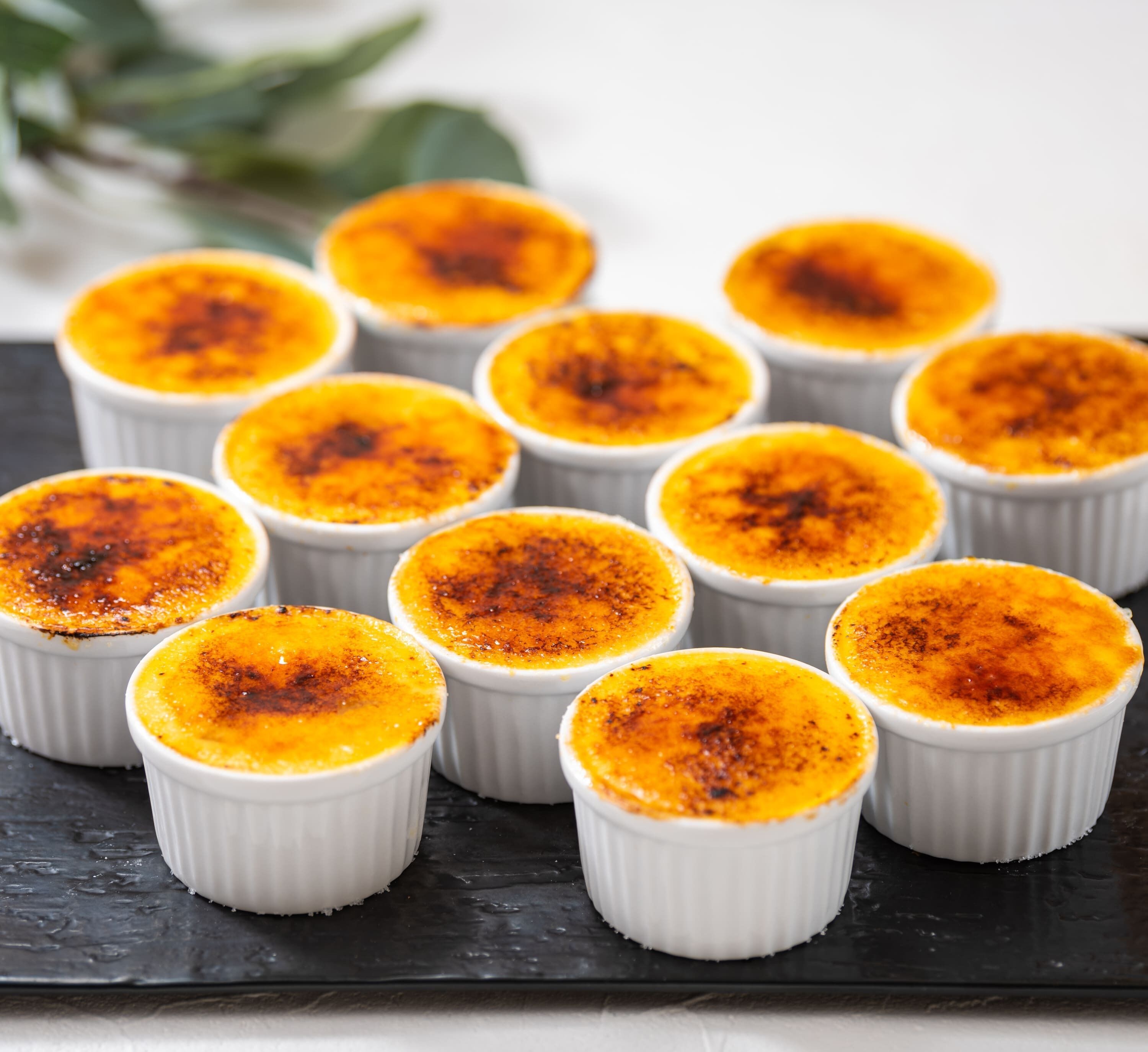Een schaal met custardbekers met een gekaramelliseerde topping, geplaatst op een donkere ondergrond.