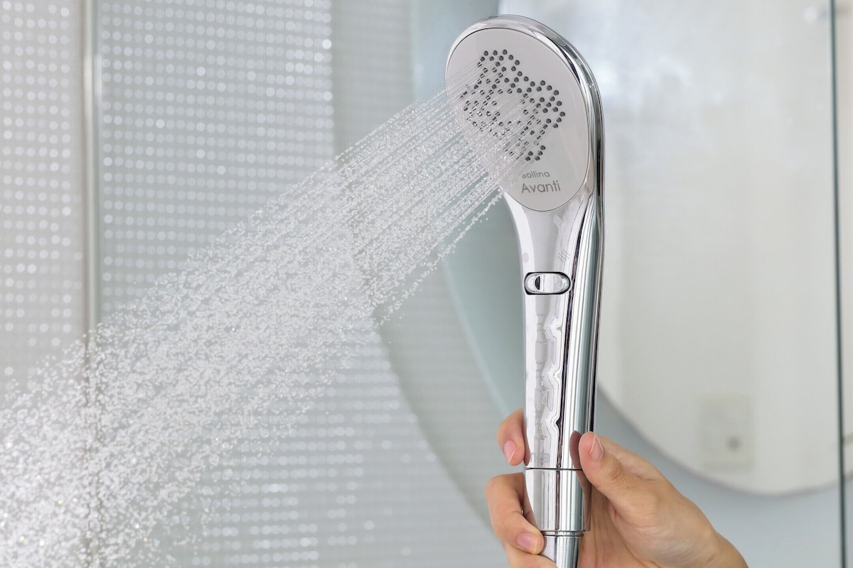 Une main tenant un pommeau de douche dont l’eau jaillit.