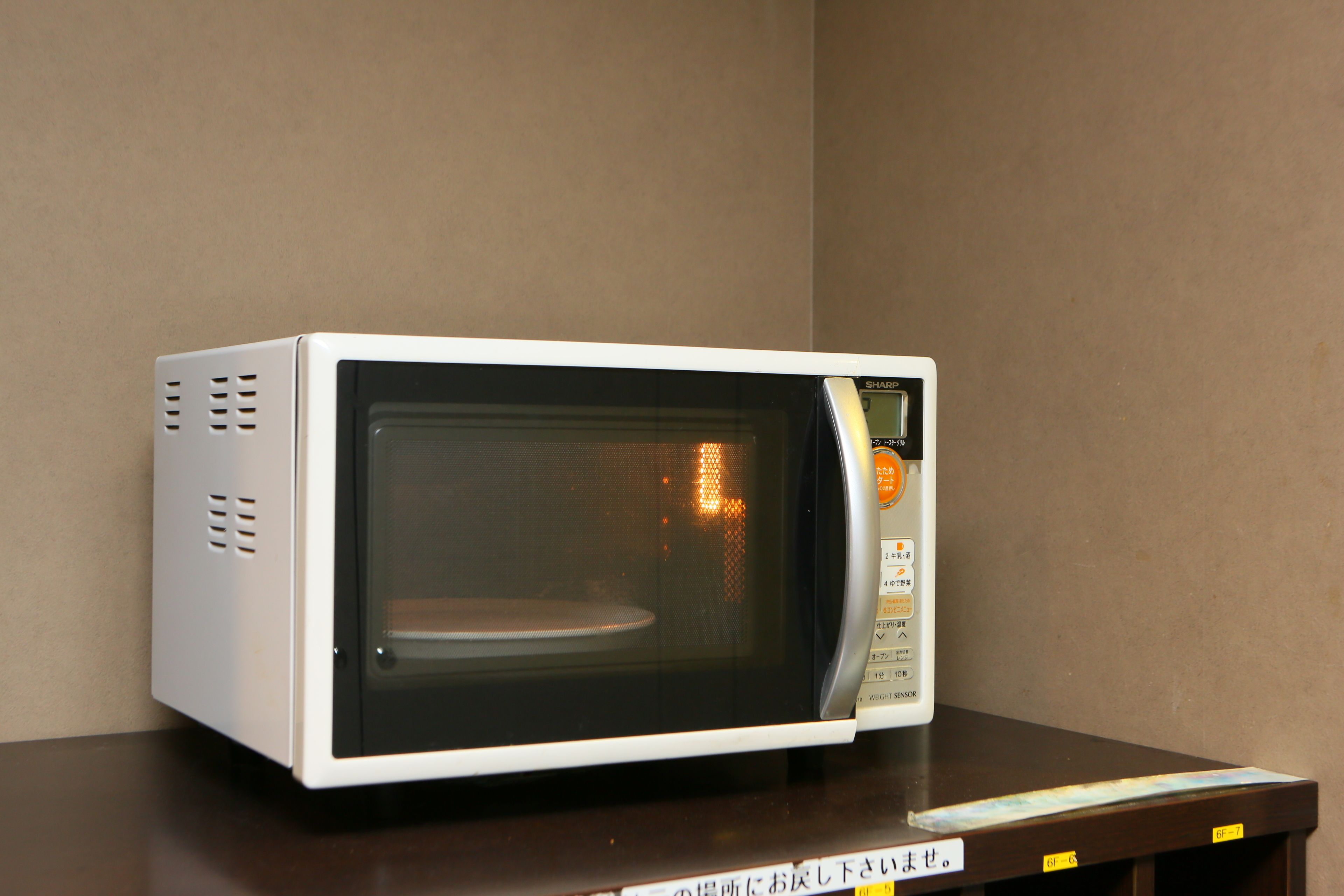 Un forno a microonde su un tavolo di legno, con una parete neutra sullo sfondo.