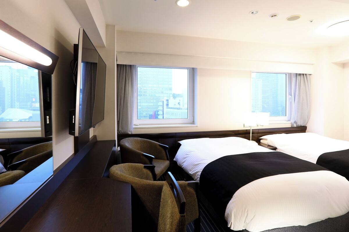 A hotel room with a bed, a chair, a desk, a TV, and a window with a city view.