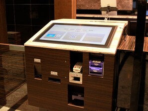 Ein Selbstbedienungskiosk mit digitalem Bildschirm, Kartenleser und Bargeldautomat in der Hotelhalle.