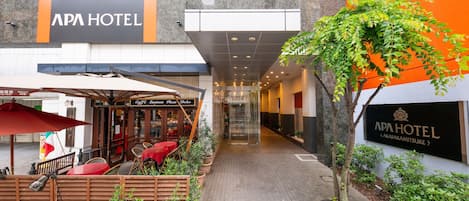 L’extérieur de l’hôtel APA présente un espace de détente extérieur abrité, des plantes en pot et un chemin dégagé menant à l’entrée.