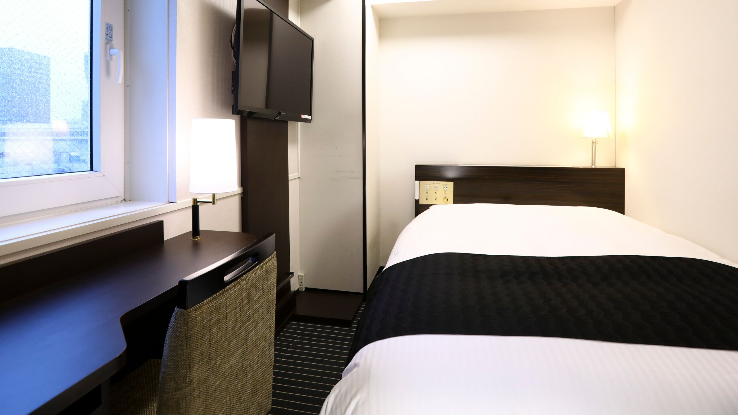 A hotel room with a bed, a desk, a TV, and a window.