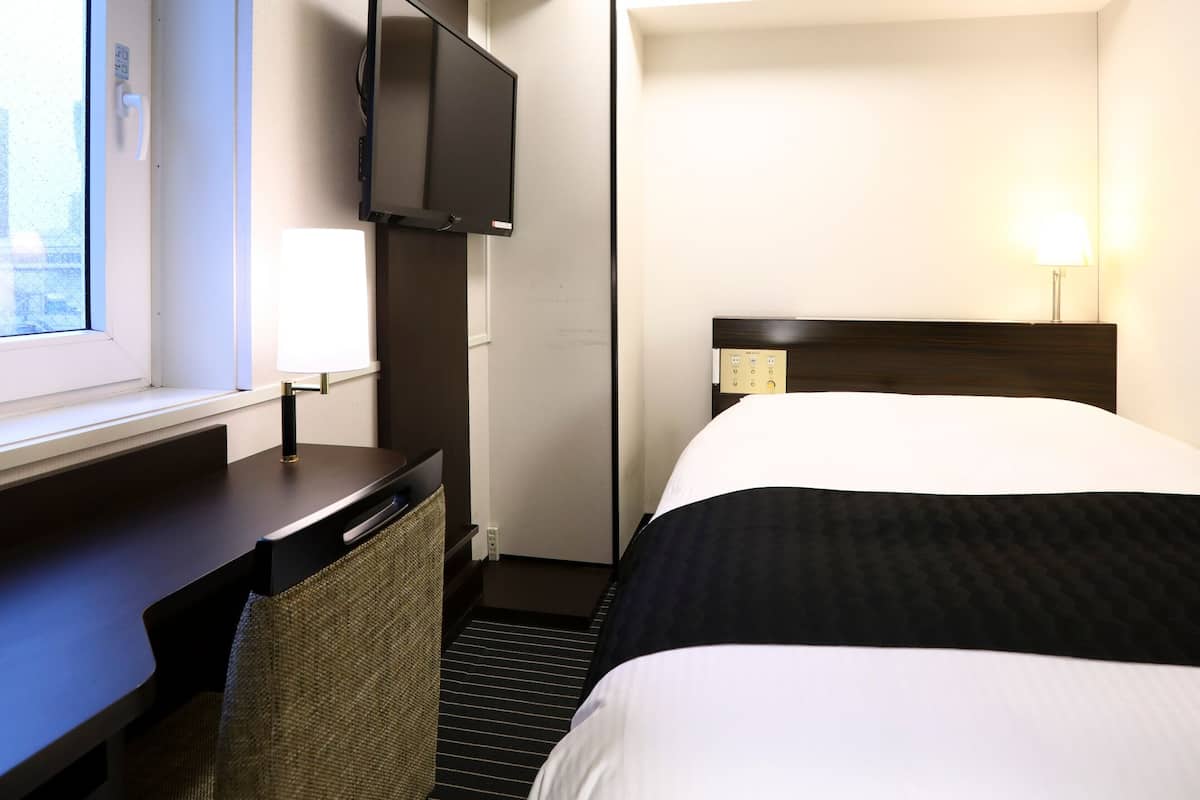 A hotel room with a bed, a desk, a TV, and a window.
