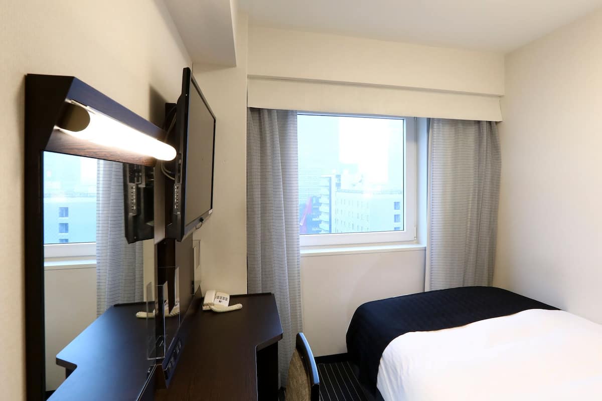A hotel room with a bed, a desk with a telephone, a television, and a window with curtains.