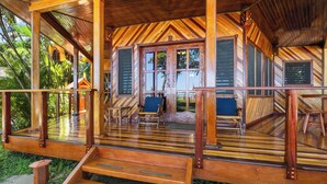Una terraza de madera con una escalera que lleva a un espacio cubierto, rodeada de abundante vegetación.