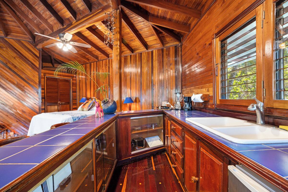 A wooden cabin interior with a kitchen area, a dining table, and a bed.