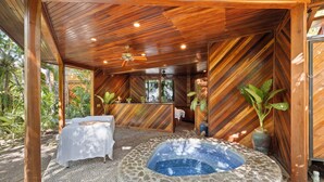 Un espacio de spa con un jacuzzi de piedra, paredes de madera y una cama con cubierta blanca.