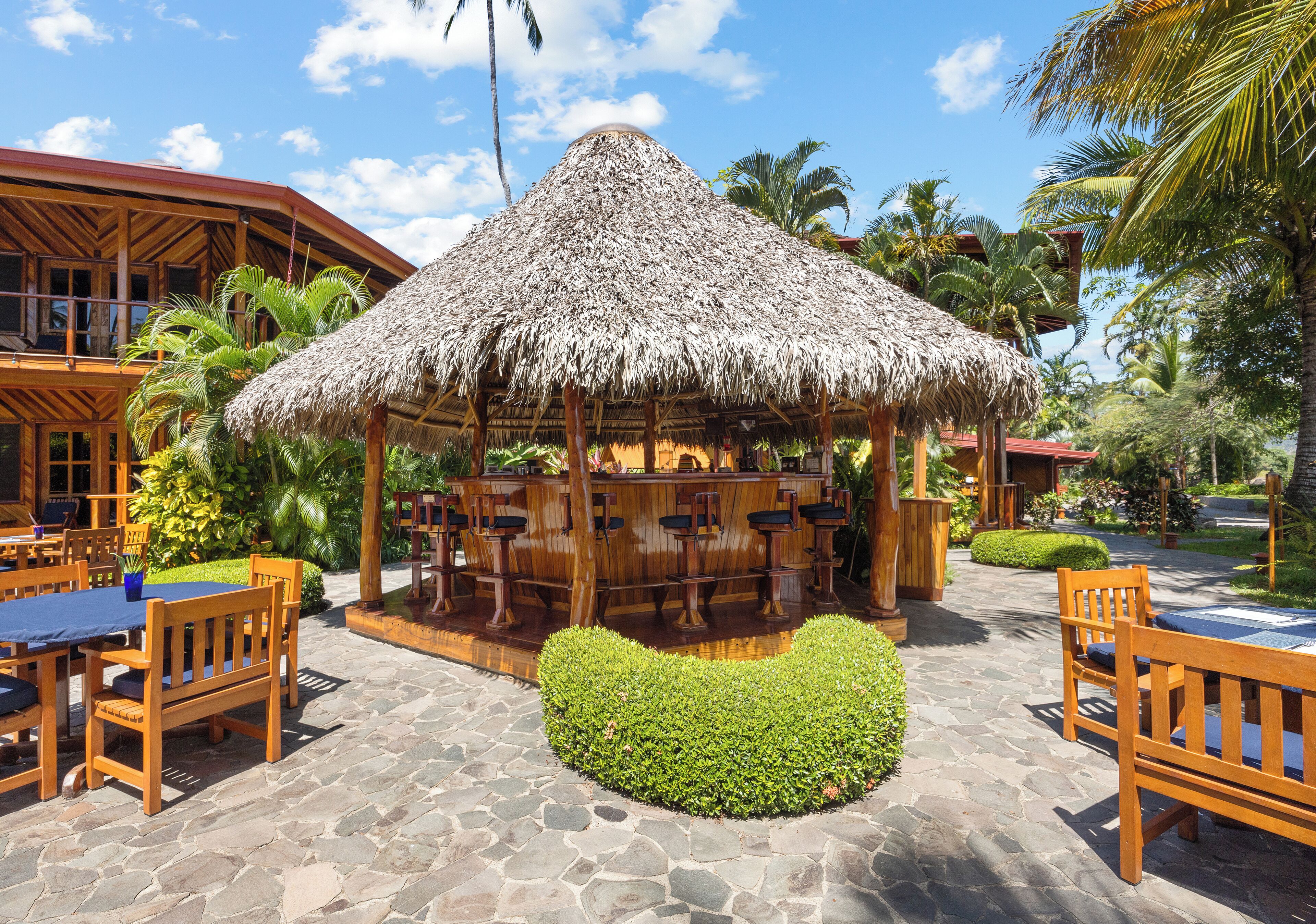 A thatched-roof outdoor bar area with wooden furniture and stone flooring.
