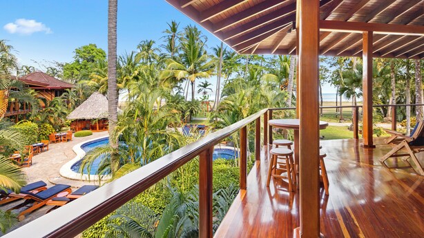 Un resort con terraza de madera, piscina y exuberante vegetación tropical.