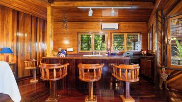 A wooden interior with a bar area, wooden chairs, a sink, and a window with a view of greenery.