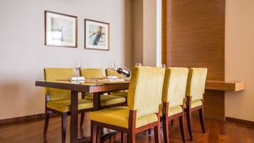 A dining area with a wooden table and yellow chairs, framed pictures on the wall, and a wooden panel on the right.