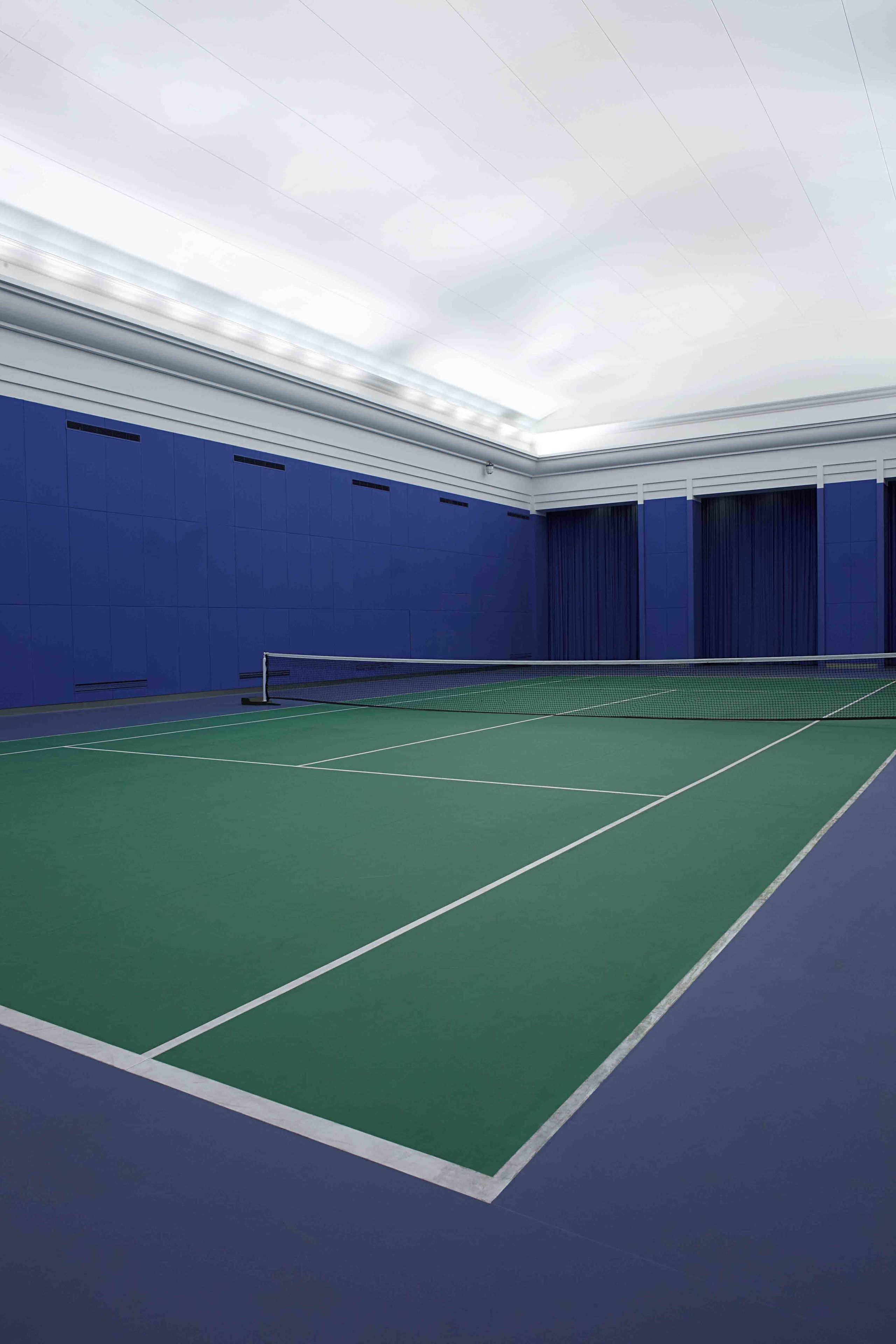 Una cancha de tenis con una red, rodeada de paredes azules y un piso verde.