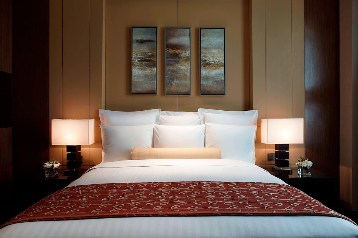 Una habitación de hotel con una cama grande, dos mesitas de noche con lámparas, y tres cuadros enmarcados en la pared.