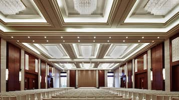Un amplio salón de conferencias con filas de sillas, un escenario y candelabros.