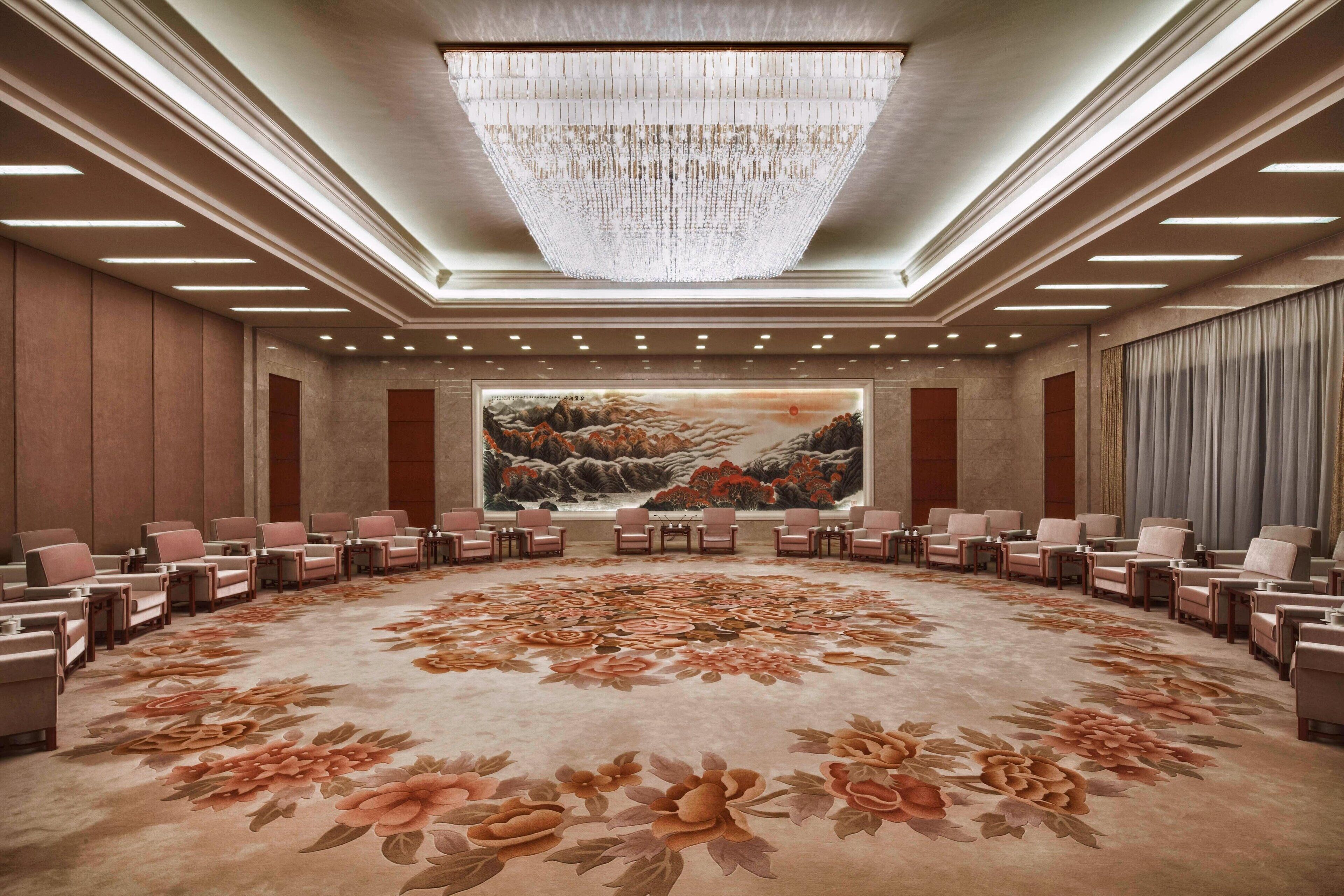 A conference room with a large floral carpet, a chandelier, and a painting on the wall.