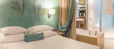 Quarto de hotel com cama, parede com mural, banheiro com banheira e chuveiro.