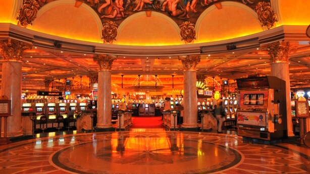 Interior de un casino con un área de juego central, elaboradas obras de arte en el techo y columnas de mármol.