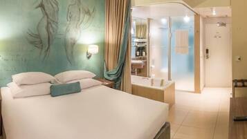 Habitación de hotel con cama, lámparas de noche, televisión, baño con ducha y espejo.