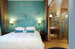 A hotel room with a bed, two bedside lamps, a nightstand, a bathroom with a sink, and a mirror.