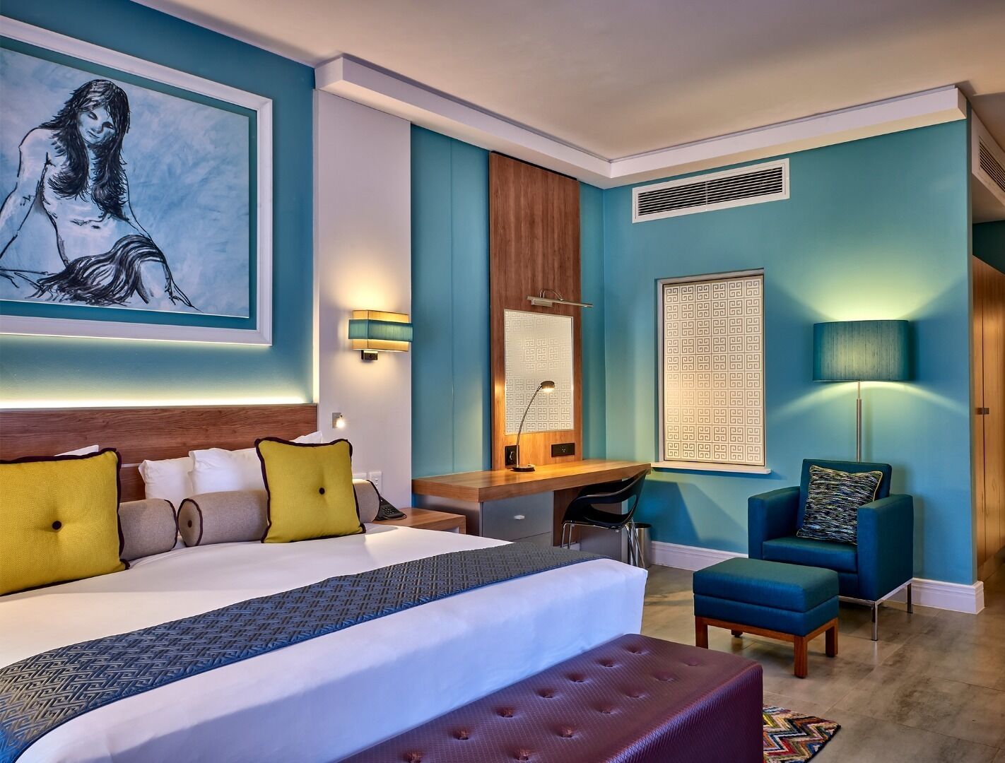 Una moderna camera d'hotel con un letto grande, una scrivania, una sedia e un muro blu decorato con opere d'arte.