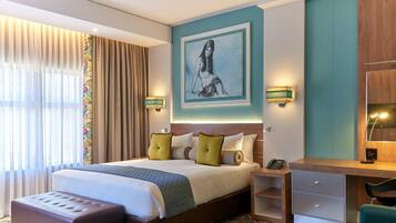 Habitación de hotel moderna con una cama grande, un escritorio y una silla. Hay un cuadro en la pared y una ventana con cortinas.