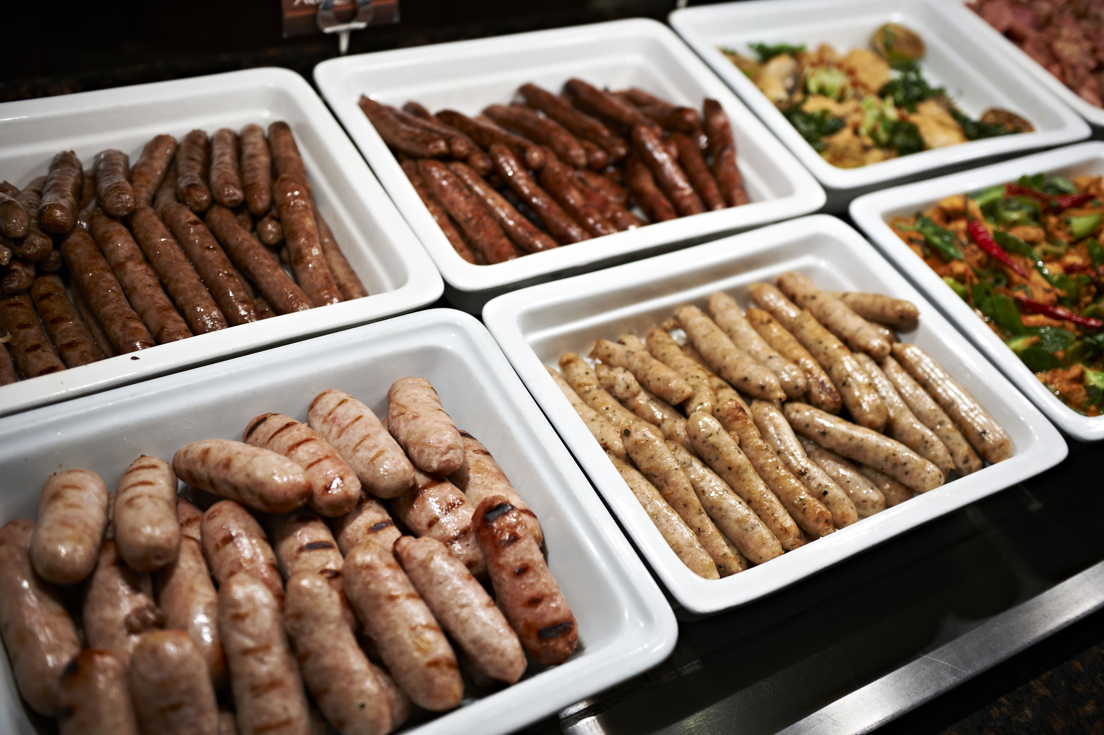 Buffet com diversos tipos de linguiça grelhada e outros pratos.