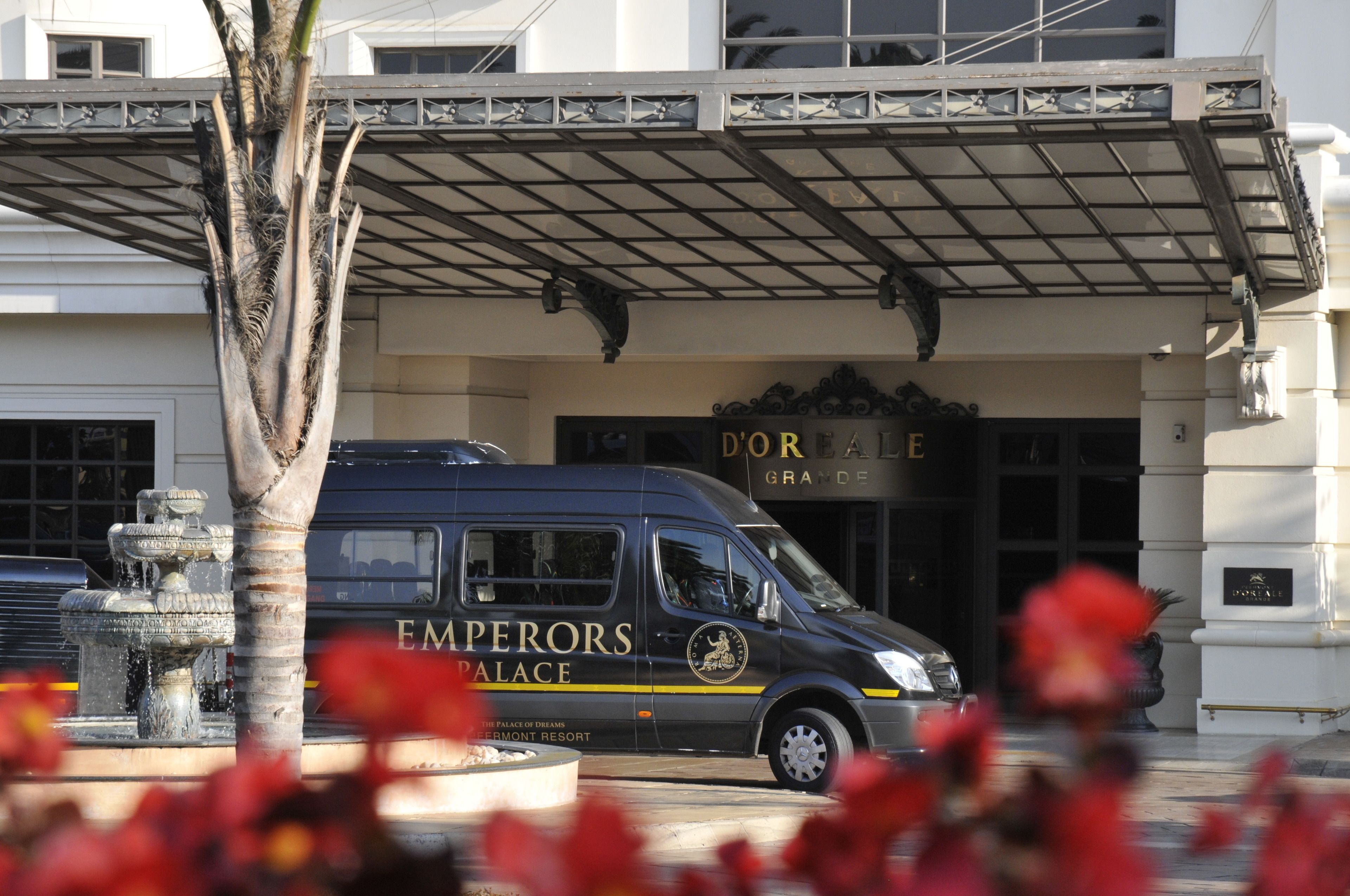 En sort varevogn med skiltene "EMPERORS PALACE" og "D'ORLE" parkeret foran en bygning med et overdækket indgangsparti.