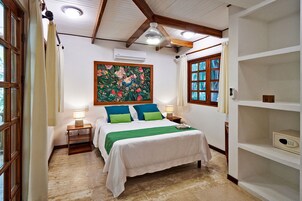 Un dormitorio con cama, mesitas de noche, un cuadro, una ventana y una estantería.