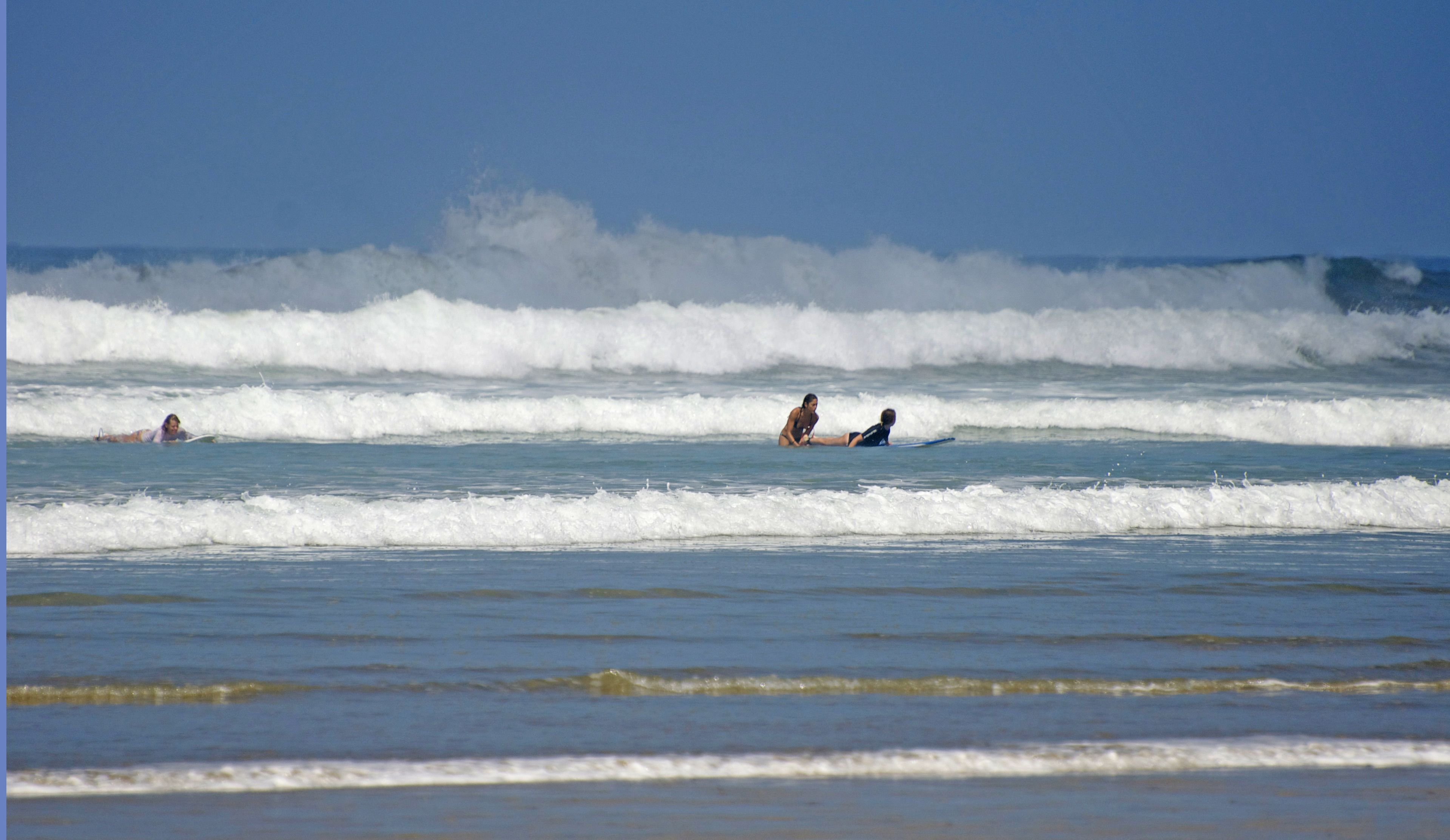 Escena de playa con olas y gente en el agua.